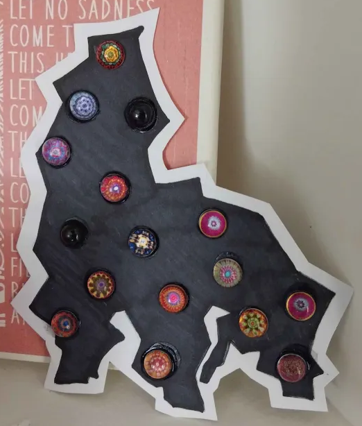 A cardstock cutout of a black amorphous creature filled in with sharpie pen and has eye-like beads glued on