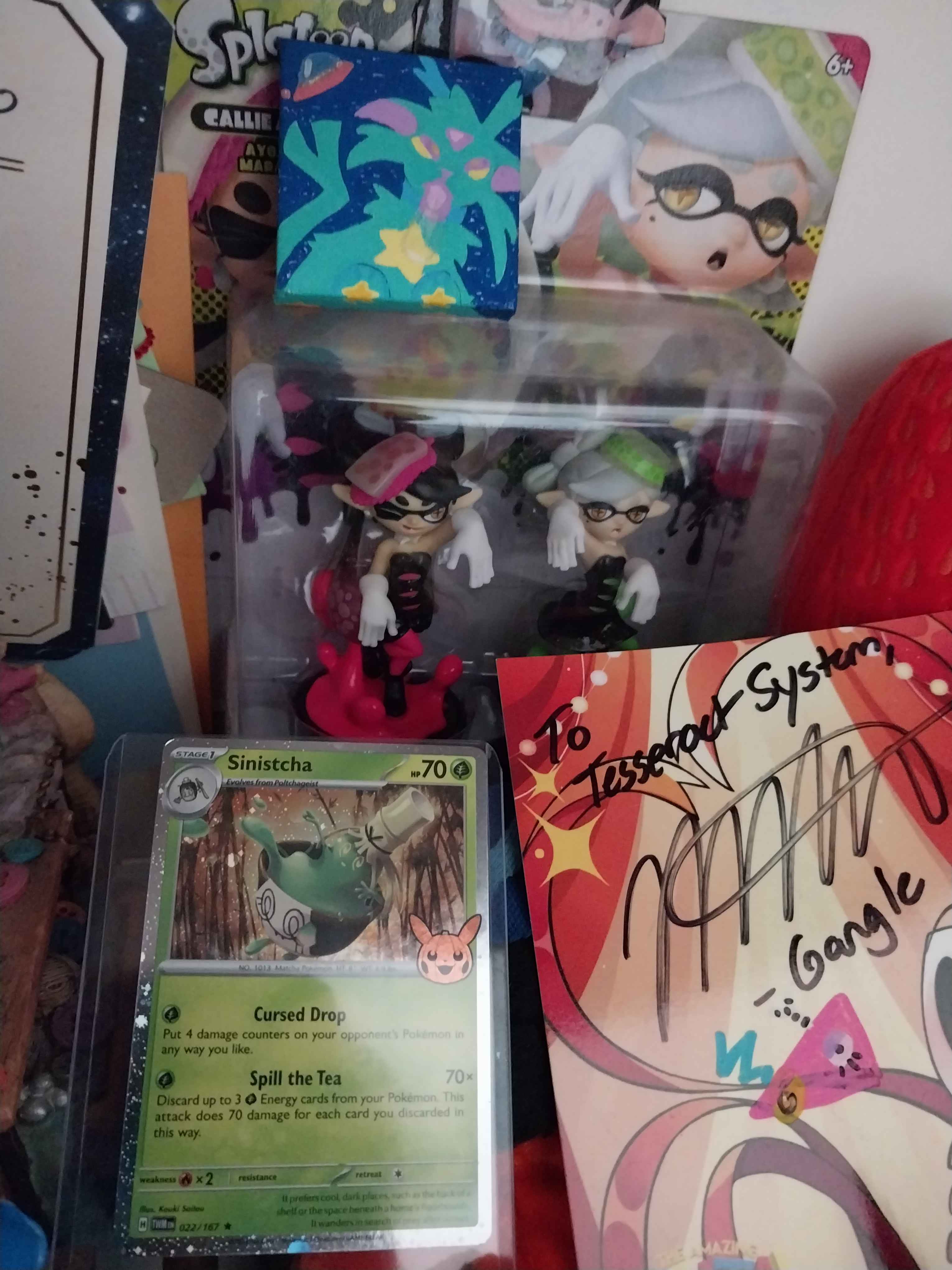 A photo of our shelf, a tiny canvas art of an Espeon is on top of a squid sisters amiibo box,there is a sleeved holo pokemon card beneath it